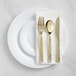 A white plastic plate with gold hammered flatware including a spoon, fork, and knife.
