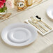 A white table setting with Visions white plastic plates and hammered flatware with a gold table setting and silverware.