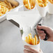 A hand using a stainless steel scoop to make french fries in a white container.