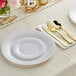 A white table setting with white wave plastic dinnerware and gold classic flatware on a white table.