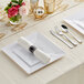 A white table setting with Visions silver and white plastic dinnerware on a table with a rose.