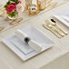 A white table setting with white plastic plates and rolled gold and silver plastic flatware.