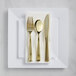 A Visions white plastic dinner plate with gold cutlery on it.