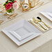 A white plastic dinner plate with gold classic flatware on a white surface.