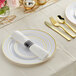 A table setting with white and gold Visions plastic plates and rolled classic flatware.