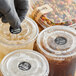 A gloved hand applying a black TamperSafe label to a plastic cup with a drink in it.