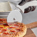 A person using a Choice 4" pizza cutter with a white handle to cut a pizza.