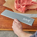 A person holding a Schraf knife with a gray polypropylene blade guard cutting meat on a cutting board.