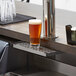 A glass of beer on a stainless steel counter with a beer tap.
