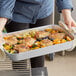 A person holding a Choice aluminum baking and roasting pan filled with chicken and vegetables.
