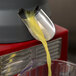 A yellow liquid being poured from a metal container into a glass.