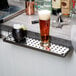 A glass of beer on a stainless steel bar counter with a metal drip tray underneath.