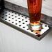 A glass of beer sits on a stainless steel beer drip tray.