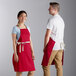 A man and woman wearing Choice red aprons standing next to each other on a counter in a professional kitchen.