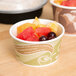 A bowl of fruit in a paper soup cup on a table.
