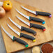A Schraf purple boning knife with a black handle in a group of knives on a cutting board.