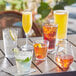 Acopa Tritan plastic stackable mixing and pint glasses filled with a variety of drinks on a table.