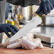 A person in yellow gloves uses a Schraf chef knife to cut a chicken.