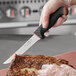 A person using a Schraf serrated utility knife with a black handle to cut meat.