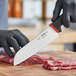A person in black gloves using a Schraf Santoku knife to cut meat on a cutting board.