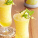 Two glasses of Monin pineapple juice with fruit on top and a green leaf.