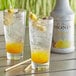 A glass of liquid with ice and pineapple and orange slices with a bottle of Monin Pineapple Fruit Puree.