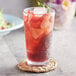 An Acopa Endure Tritan plastic highball glass filled with a red drink, ice, and strawberries.
