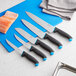 A Schraf serrated utility knife with a blue handle in a group of knives on a cutting board.
