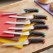 A Schraf serrated bread knife with a blue handle in a group of knives on a red surface.