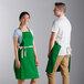 A man and woman wearing Choice kelly green bib aprons with natural webbing accents.