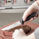 A person using a Schraf utility knife with a black TPRgrip handle to cut a piece of meat.