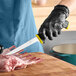A person in a black glove using a Schraf narrow stiff boning knife to cut meat on a wooden surface.