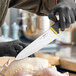 A person in gloves using a Schraf chef knife with a yellow TPR grip to cut a chicken.