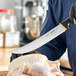 A person using a Schraf Cimeter knife with a yellow handle to cut a raw chicken.
