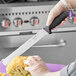A person in a glove using a Schraf serrated slicing knife with a purple handle to cut cauliflower.