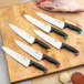 A Schraf chef knife with a purple handle on a cutting board with other knives.