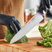 A black-gloved hand uses a Schraf Chef Knife to cut broccoli.