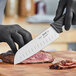 A person in black gloves uses a Schraf Santoku knife to cut a piece of meat.