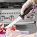 A person in gloves using a Schraf serrated utility knife with a purple and black handle to cut a pomegranate.