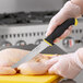 A person in gloves uses a Schraf serrated utility knife with a yellow TPRgrip handle to cut a chicken on a cutting board.