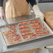 A woman using tongs to place bacon on a Choice chrome footed cooling rack.