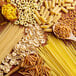 A wooden surface with a spoonful of Barilla Gluten-Free Elbow Pasta and a group of different types of pasta.