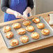 A person in a blue apron uses a pastry bag to frost pastries on a Choice chrome plated cooling rack.