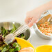 A hand using clear Thunder Group tongs to serve salad from a yellow bowl.