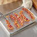 A Choice chrome plated footed wire cooling rack with bacon on it.