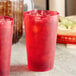Two red Choice plastic tumblers filled with ice and drinks on a counter.