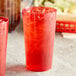 Two red Choice plastic tumblers filled with ice on a table.
