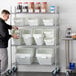 A man standing next to a shelf of Baker's Mark white plastic ingredient bins with clear flip lids.