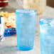 Two blue Choice plastic tumblers filled with ice on a table with a blue bowl of food.