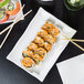 A rectangular white porcelain platter with a bamboo pattern holding sushi with chopsticks.